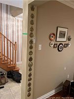 Wall-mounted display showing a vertical row of sixteen horse brasses of various designs and sizes.