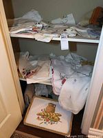 Three shelves showing embroidered linens and decorative tray at bottom
