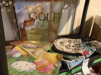 Photo showing several colorful seasonal garden flags spread on a surface and a black metal stand for flag holding.