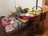 Photo of wooden sewing box filled with yarn balls, tins, and trays containing sewing supplies and notions.