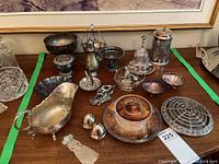 Overview photo showing multiple silver plate and metal serving pieces arranged on a table, including a gravy boat, bowls, baskets, salt and pepper shakers, and glass items