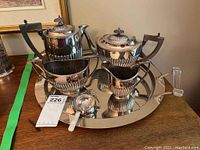 Full view of silver plate tea and coffee service displayed on stainless steel tray with lucite handles, includes cream, sugar, and tea strainer.