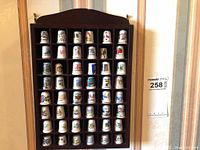 Front view of 48 ceramic thimbles displayed in wooden shelving, showing colorful imprints including landmarks and flowers.
