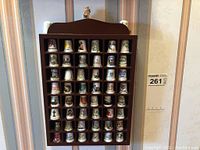 Front view of the brown wooden shelving unit filled with 51 decorative thimbles arranged in rows and columns, displaying various colorful designs and place names.