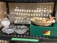 Multiple glass vases, clear glass serving platters, white ceramic pitcher, and Fritz and Floyd serving tray with bunny figurine and floral painted surface on green box.