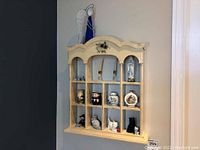 Wooden wall shelf with floral design mounted on wall holding various small figurines and decorative jars.