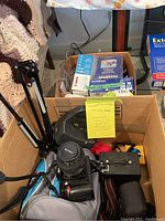 Overhead view of cardboard box containing tripod, soft cases, camera boxes and Nikon D70 setup