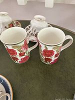 Two Royal Albert Moss Rose styled teacups with red rose floral pattern and green rim.