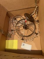 Chandelier packed in a cardboard box showing the top frame, ceiling canopy, wiring, and crystal prisms inside the box.
