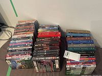 Photo showing stacks of DVDs and VHS tapes arranged in three piles on a flat surface. Titles of West Wing and others visible.