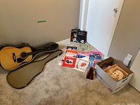 Full view of guitar in open case beside metronome, loose sheet music and box of books