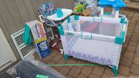 Wide view showing Peg Perego highchair, Evenflo Happy Camper play yard, and safety gate alongside boxed Pedigo item and other toys.