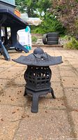 Side angle view of black metal outdoor candle lantern on paved surface showing hexagonal design, legs and textured roof.
