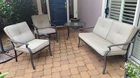 Photo showing full outdoor set: loveseat, two chairs with cushions, and glass-top table on brick patio.
