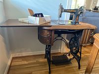 Side view of vintage Raymond sewing machine mounted on full wooden treadle table with drawers and side extension open
