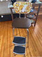 Full view of vintage Nortex stool showing floral vinyl backrest, padded brown vinyl seat and two folding metal steps with black grips.