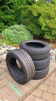 Four tires stacked on patio pavers, one leaning against stack