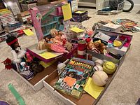 Overview of the lot showing Barbie dolls, other small dolls, toys, piggy banks, baseballs, puzzle box and cards.