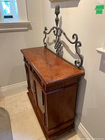 Full view of the wood cabinet with metal decorative backpiece on top, showing front and side.