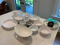 Full view of all ceramic and glass kitchenware on countertop including covered dishes, ramekins, pie plates, jars with lids.