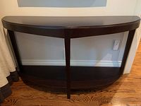 Front view of the demi lune console table showing the shape, color, and supporting legs against a wall.