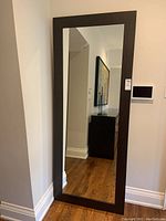 Full view of the mirror standing against a wall in a corner, showing the proportion and color of the frame in relation to wood floor and baseboard.