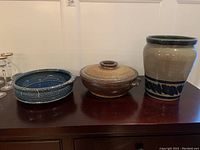 Main photo showing all three pottery pieces, two round dishes and one large vase, on a wooden surface.