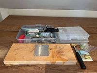 Photo showing wooden board with attached metal anvil and two plastic containers behind with jewellery supplies and hammer.
