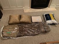 Photo of the two brown patterned cushions, cream-colored weighted blanket cover in sealed packaging, brown/gold striped duvet cover in sealed plastic, and a third cream-colored item in sealed packaging.