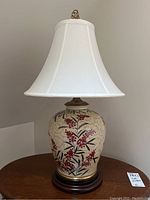 Full view of ceramic ginger jar style table lamp with white fabric shade, showing red berries and green leaves pattern on cream crackled base and wood stand.