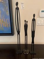 Three metal sculptural figures of humans in black, abstract elongated forms with varying heights: 17, 19.5, and 24 inches.