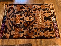 Full view of the Peruvian area rug showing overall design and colors including black, brown, tan, cream, and colorful geometric border patterns with fringe.