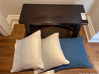 Top view of dark wood bench with three linen pillows on top: two light striped and one solid blue.