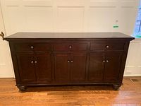 Front view of sideboard showing three drawers above four paneled doors and bun feet