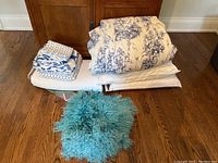 Stacked bedding items and teal shaggy accent pillow on hardwood floor
