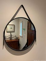 Circular mirror hung on wall with black leather belt, showing the mirror's round shape and belt hanger.
