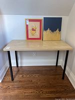 Full view of the birch veneer table with two framed artworks placed on top to show scale and setting.