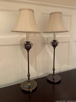 Photo of two matching table lamps on a dark wooden surface against a white paneled wall, showing overall size and design.