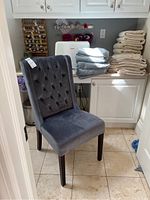 Blue velvet upholstered chair with tufted high back and dark wooden legs, positioned near countertop with towels.