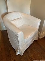 Side view of white upholstered armchair with loose back and seat cushions, textile slipcover with skirted base.
