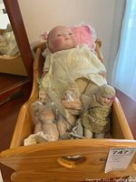 Wooden cradle containing five porcelain dolls, some disassembled, with pink bedding inside the cradle.
