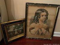 Two vintage framed pictures: a portrait of a young girl with curly hair, and a landscape scene with figures and dogs