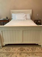 Front view of cream sleigh bed with white bed linens and pillows.