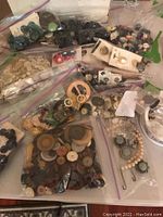 Wide view of collection of bags and box containing various buttons, button covers, and belt buckles in multiple materials and styles.