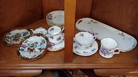 Photo showing various tea plates, cups, and saucers arranged on a wooden shelf.