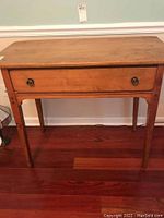 Front view of vintage maple wood desk showing single drawer with round metal pulls and tapering legs.