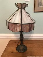 Full view of lamp showing metal base and multi-paneled leaded glass shade with scalloped edges