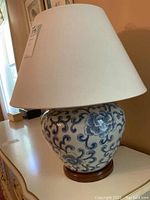 Full view of lamp showing blue-and-white ginger jar base and white linen shade on wooden stand.