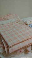 Stack of bedding including pink checked sheet or pillowcase on top, with other bedding underneath in white and cream tones.