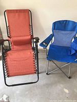 Photo shows two folding chairs: an orange nylon mesh lounge chair with padded armrests and a blue nylon camp chair with mesh panel and cup holder